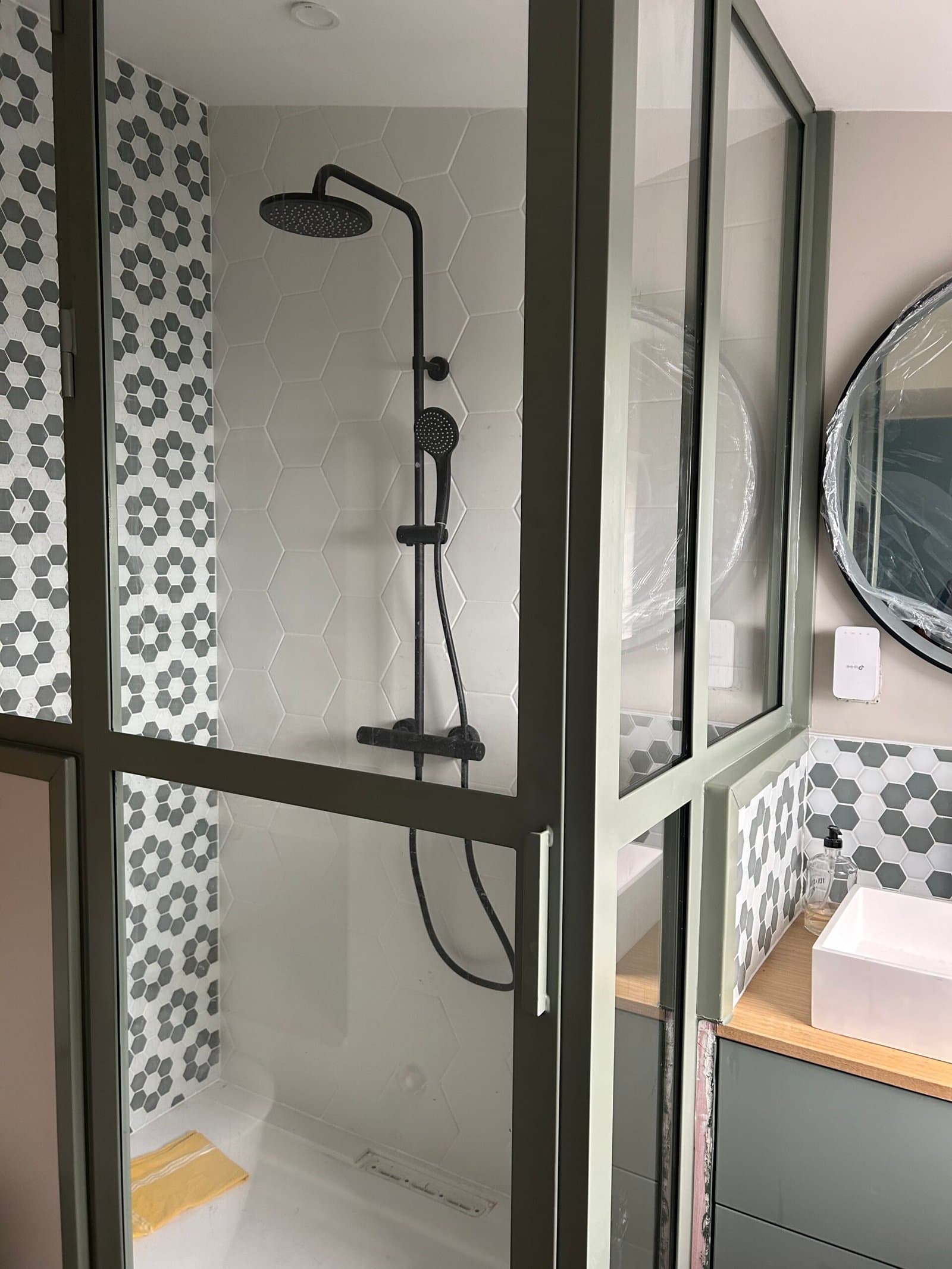 Salle de bain rénovée avec verrière d'atelier, douche carrelée hexagonale et vasque sur plan bois