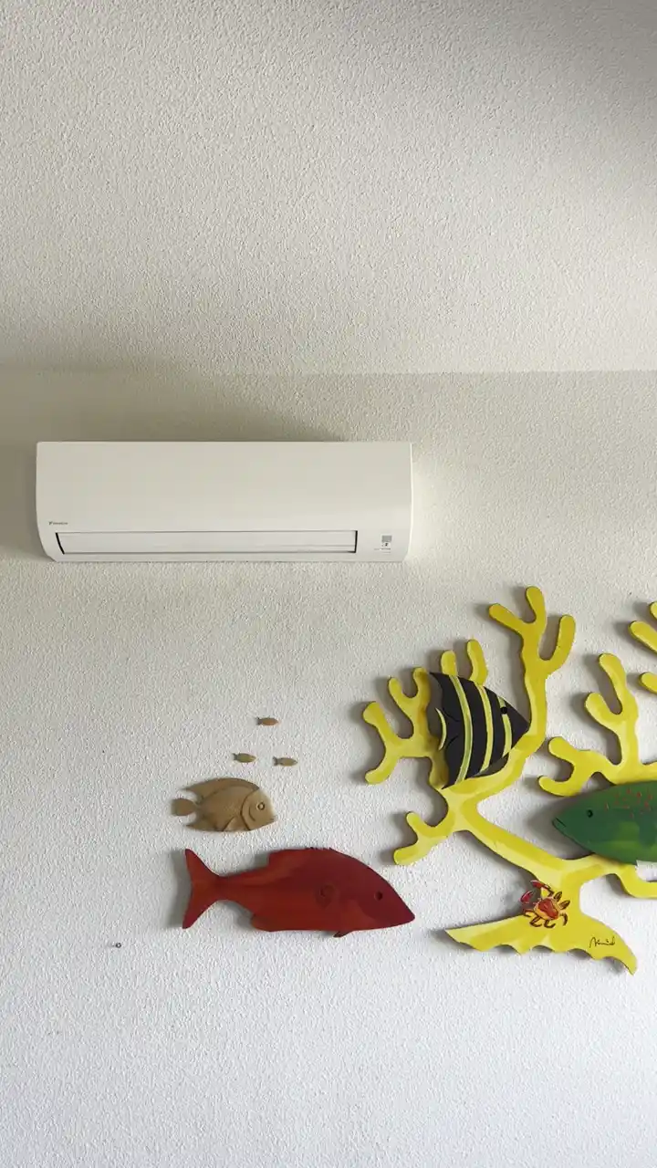 Unité intérieure de climatisation réversible murale installée en hauteur dans la pièce à vivre d'un appartement à Saint-Pierre-la-Mer