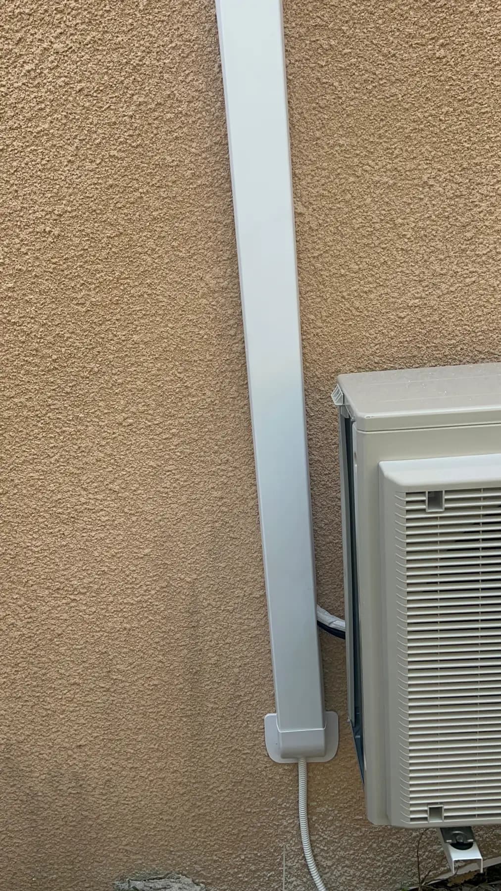 Unité extérieure de climatisation fixée en façade, liaisons protégées par une goulotte verticale, installation A2C Plomberie à Saint-Pierre-la-Mer