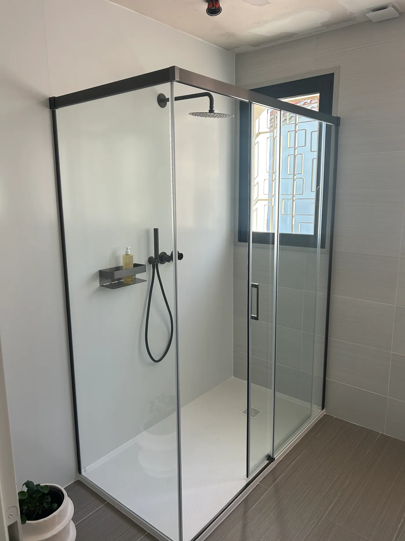 Douche d'angle avec receveur extra-plat, paroi vitrée coulissante et robinetterie noir mat