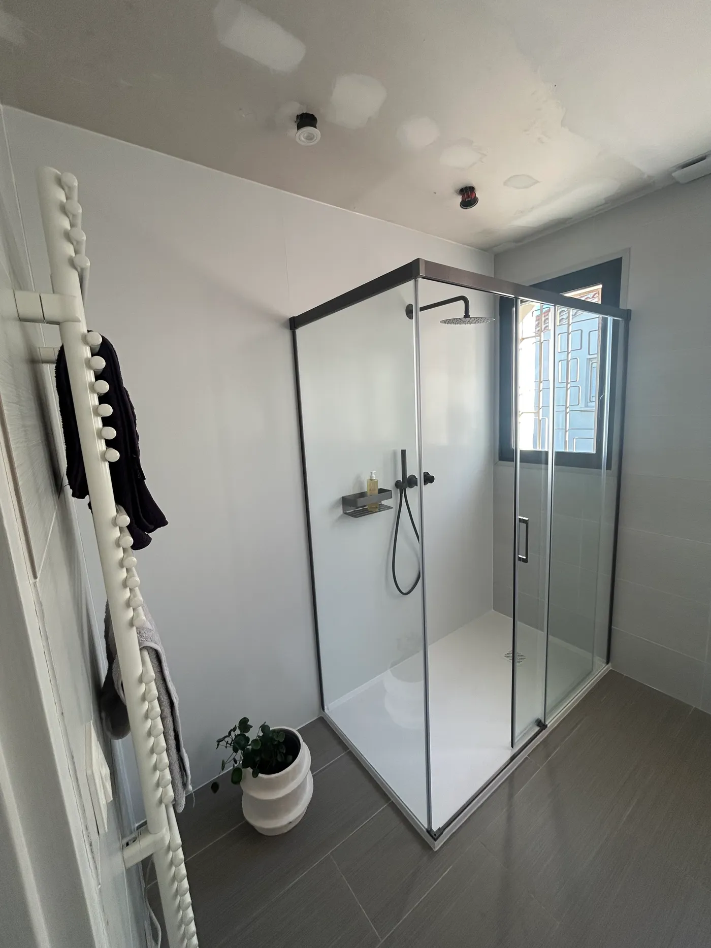 Salle de bain rénovée avec sèche-serviettes design et sol carrelé gris, par A2C Plomberie