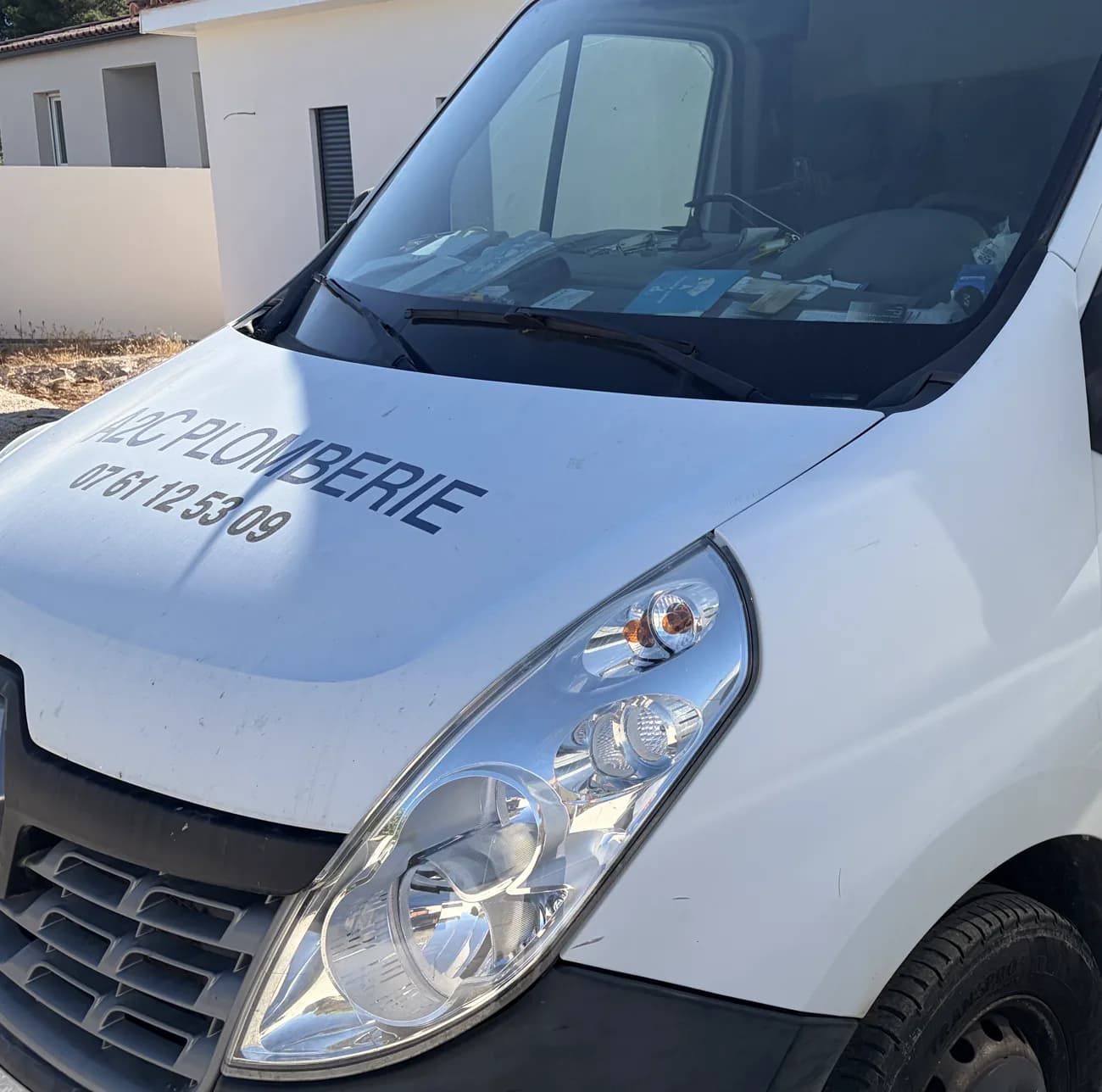 Véhicule utilitaire A2C Plomberie portant le nom de l'entreprise et le numéro de téléphone, stationné devant une maison