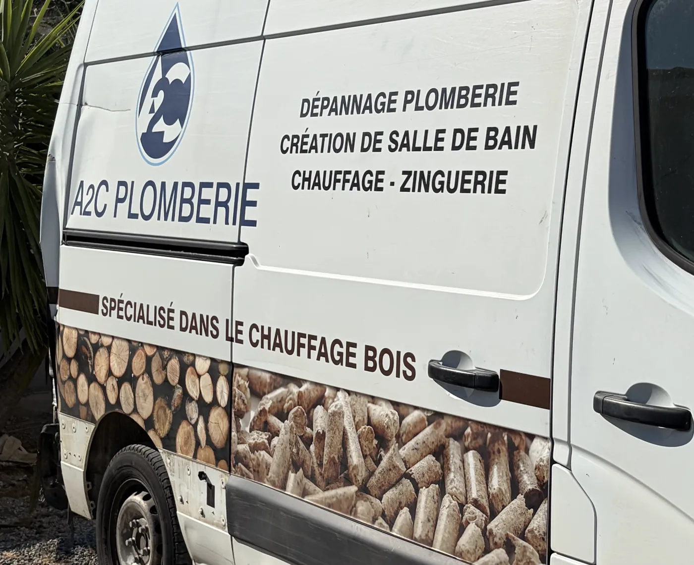 Flanc du véhicule A2C Plomberie listant les prestations dépannage plomberie, création de salle de bain, chauffage et zinguerie, avec la mention Spécialisé dans le chauffage bois