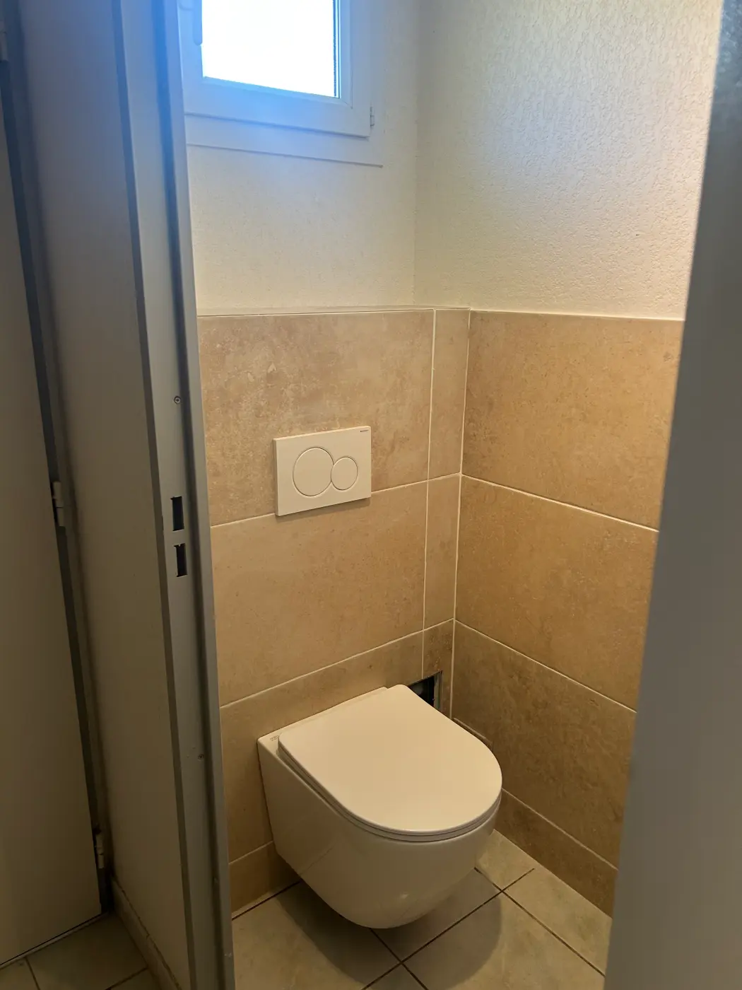 WC suspendu sur bâti-support habillé de carrelage beige façon pierre, avec plaque de commande double touche